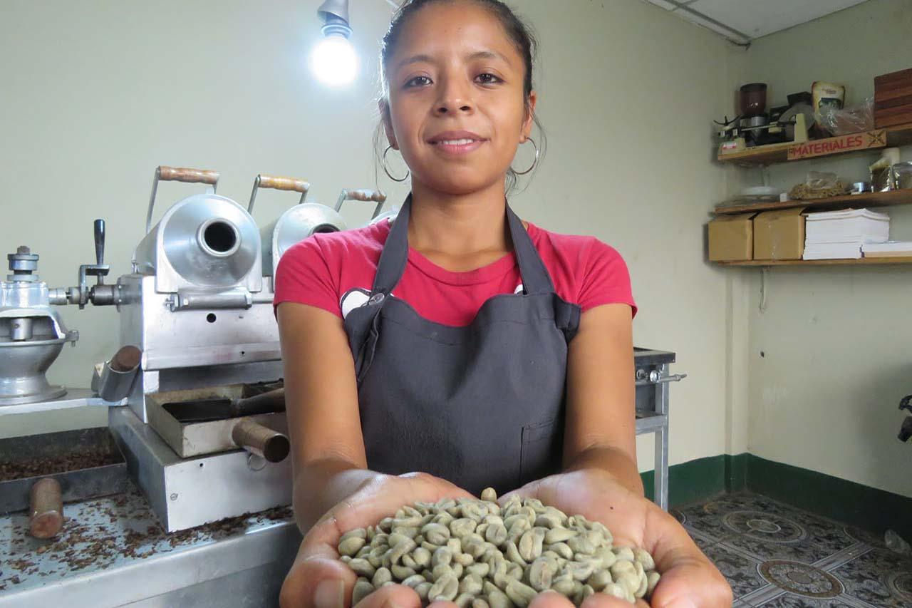 Lächelnde Mitarbeiterin von Cosatin hält eine Handvoll roher Kaffeebohnen