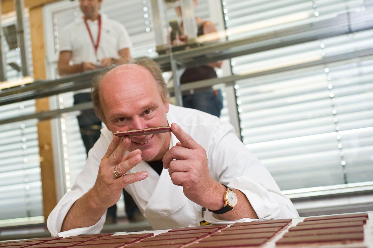 Josef Zotter hält lächelnd eine aufgeschnittene Schokoladentafel in der Manufaktur