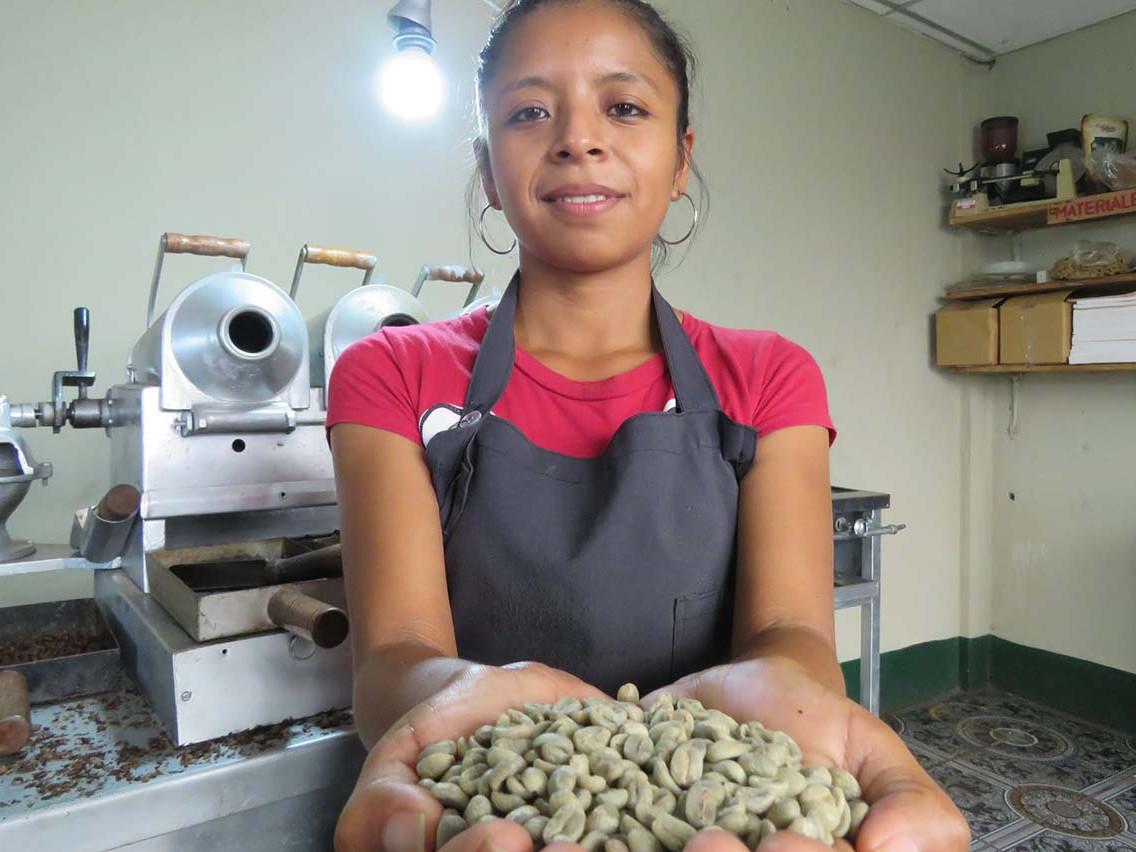 Lächelnde Mitarbeiterin von Cosatin mit den Händen voll getrockneter Kaffeebohnen
